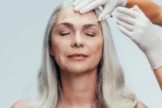 Elegant mature woman receiving premium neurotoxin injection treatment at Kansas City's Aesthetics For Women clinic. Expert Missouri medical professional administering precise anti-aging therapy for smoother skin and reduced wrinkles. Experience the gold s