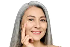 Confident mature woman with beautiful silver hair applying under-eye treatment, demonstrating effective Kansas City anti-aging solutions from Aesthetics For Women. Experience premium skincare services in KC for mature skin, including Missouri's finest eye